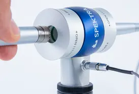 One hand holds a microphone, which is inserted into the electro-acoustic coupler for calibration.