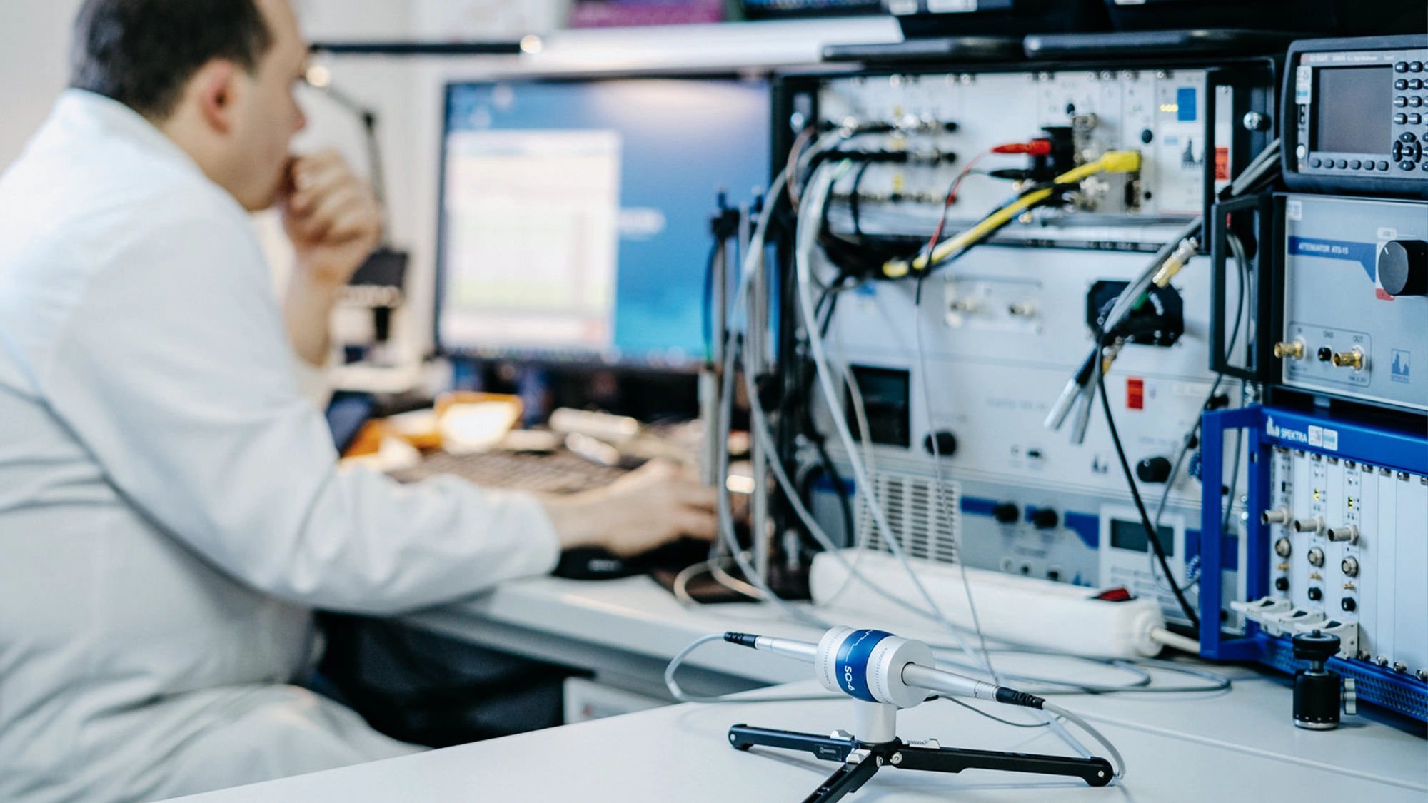 Calibration of measurement microphones in the right foreground in an acoustics laboratory with a technician in the background on the left.
